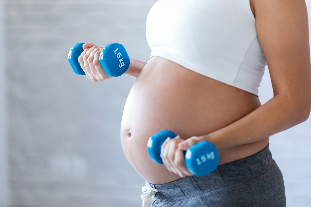 Close up of Pregnant woman's belly working out with weights